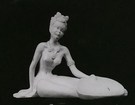 Seated lady figurine made of chalkware with hair tied up and holding bowl in left hand